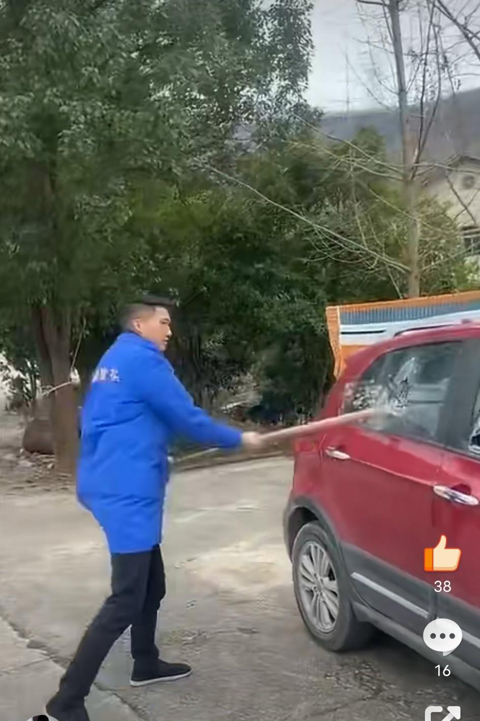 这位身着“某某烟花”公司工作服的男子，手持二齿钉耙，对着一台停在路边的湘K哈弗车