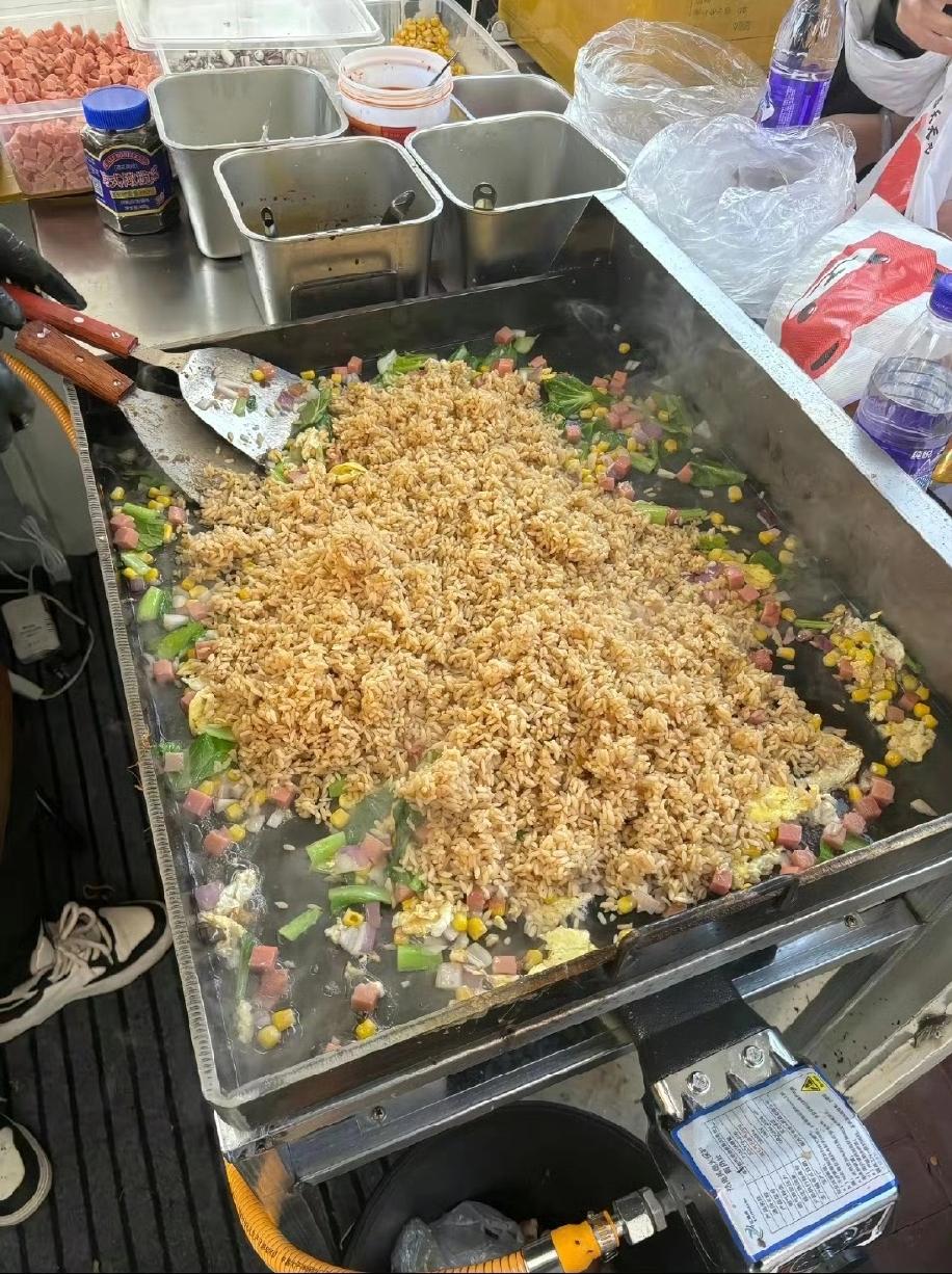 最近吉林四平的街头，一个炒饭摊位前排起了长队。摊主是位中年大叔，他握着铁铲的手被