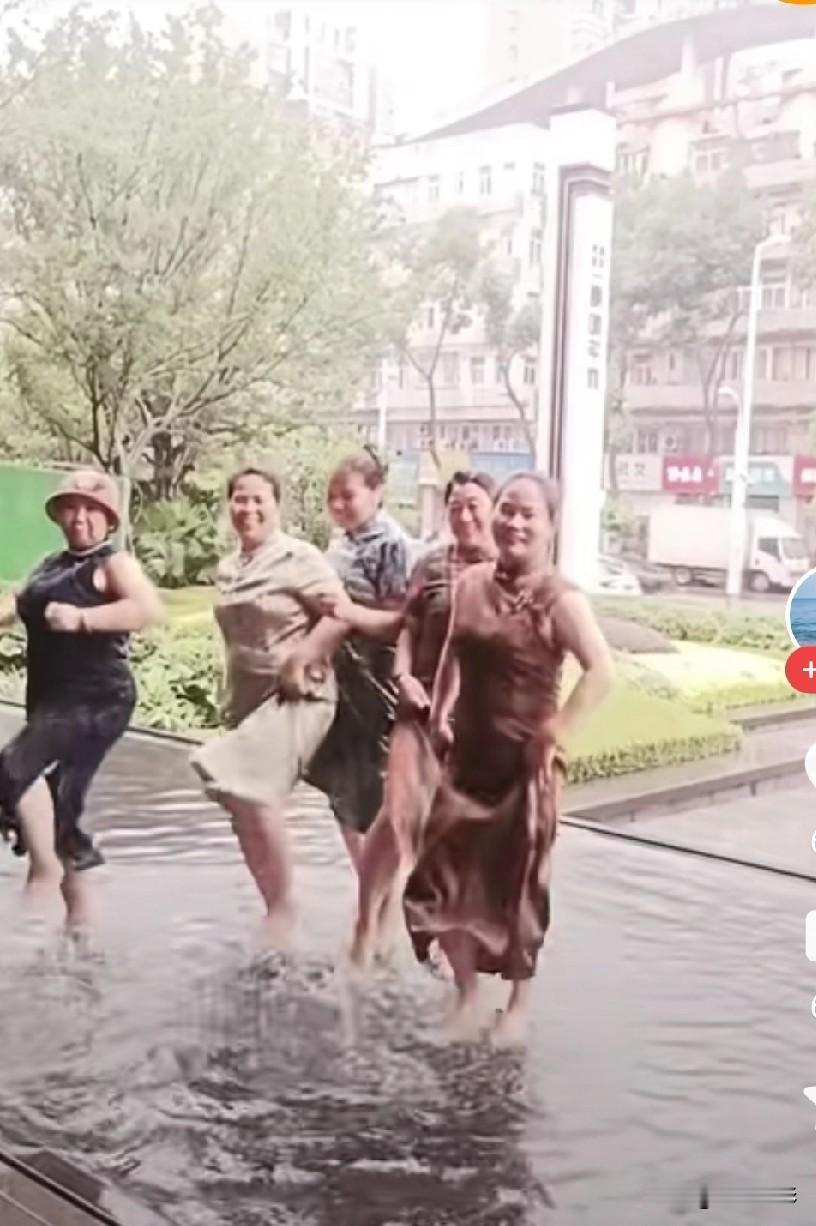 几个六，七十岁的大妈，在城市路边的水池里，满脸笑容地踩着音乐节奏开心地蹦着。