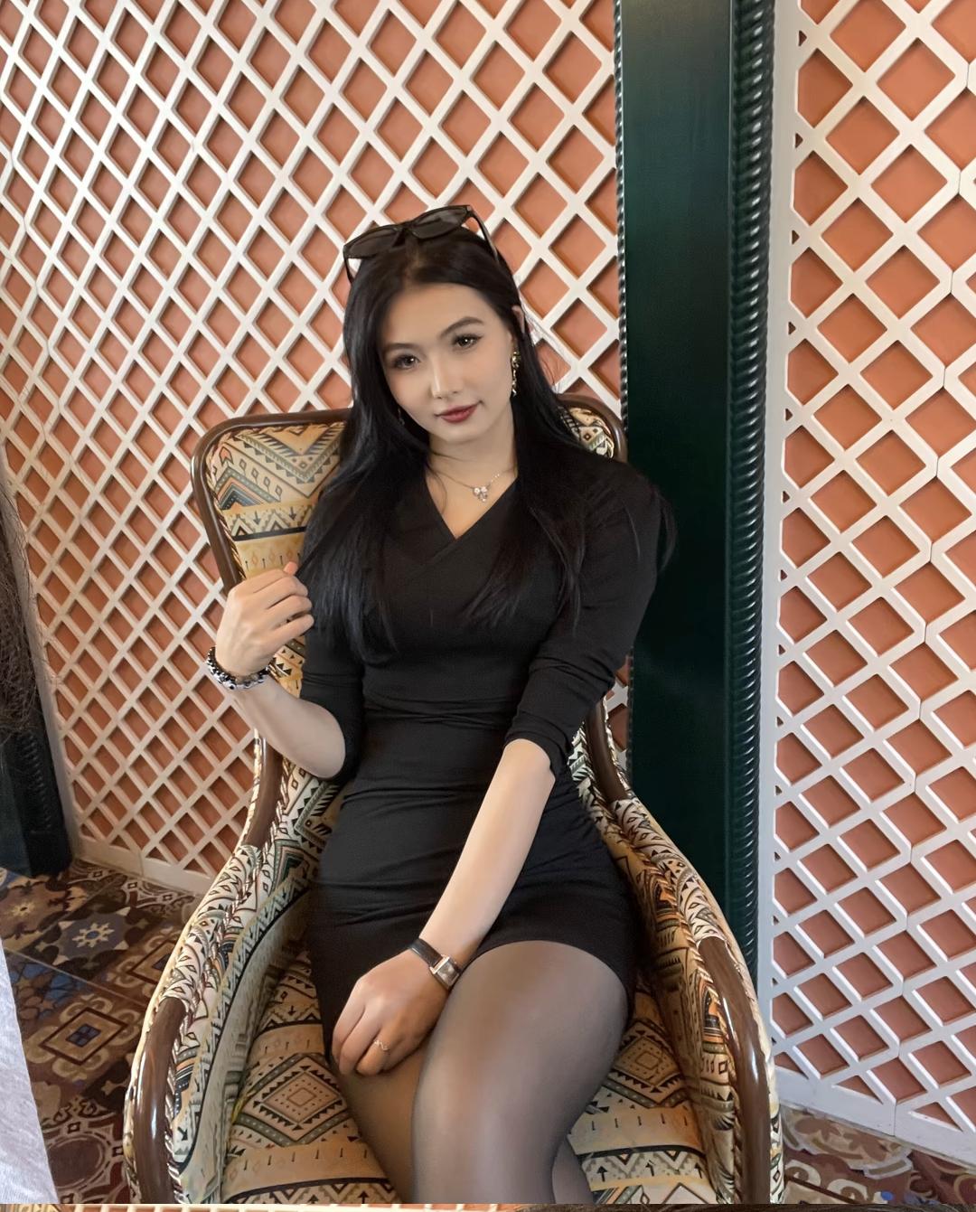 优雅黑裙，复古椅背，时尚眼镜，精致妆容，自信微笑。