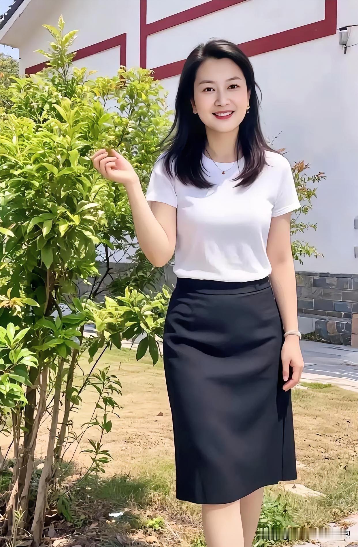 素白上衣衬清新，墨裙曳地显温婉。她立绿意间，指尖轻触叶梢，笑靥如阳光洒落，将日常