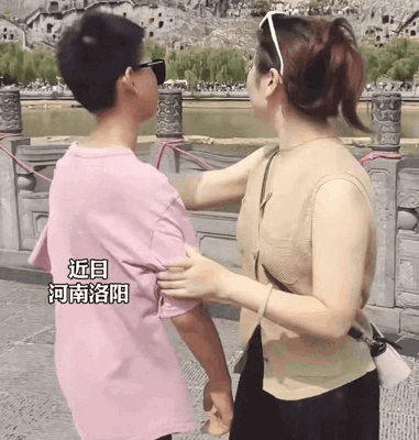 河南洛阳，一景区门口妈妈满心欢喜拉着儿子合影，熟练比出经典耶耶手势，满心期待拍出