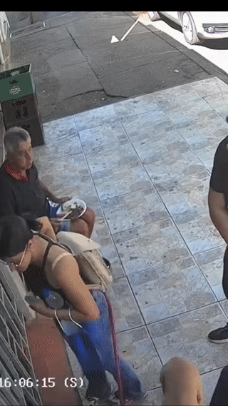 国外一位大叔正坐在店门口吃牛排。一名年轻女子牵着她的狗从大叔身边经过。大叔看