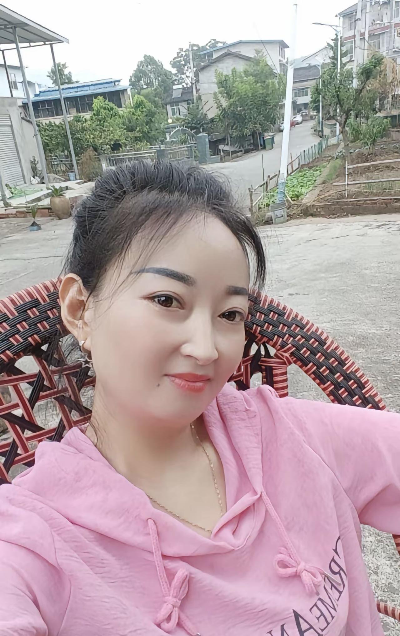 农村的新媳妇在农村小院，她身着粉色连帽衫，坐在藤椅上，眉眼间藏着初来乍到的羞涩