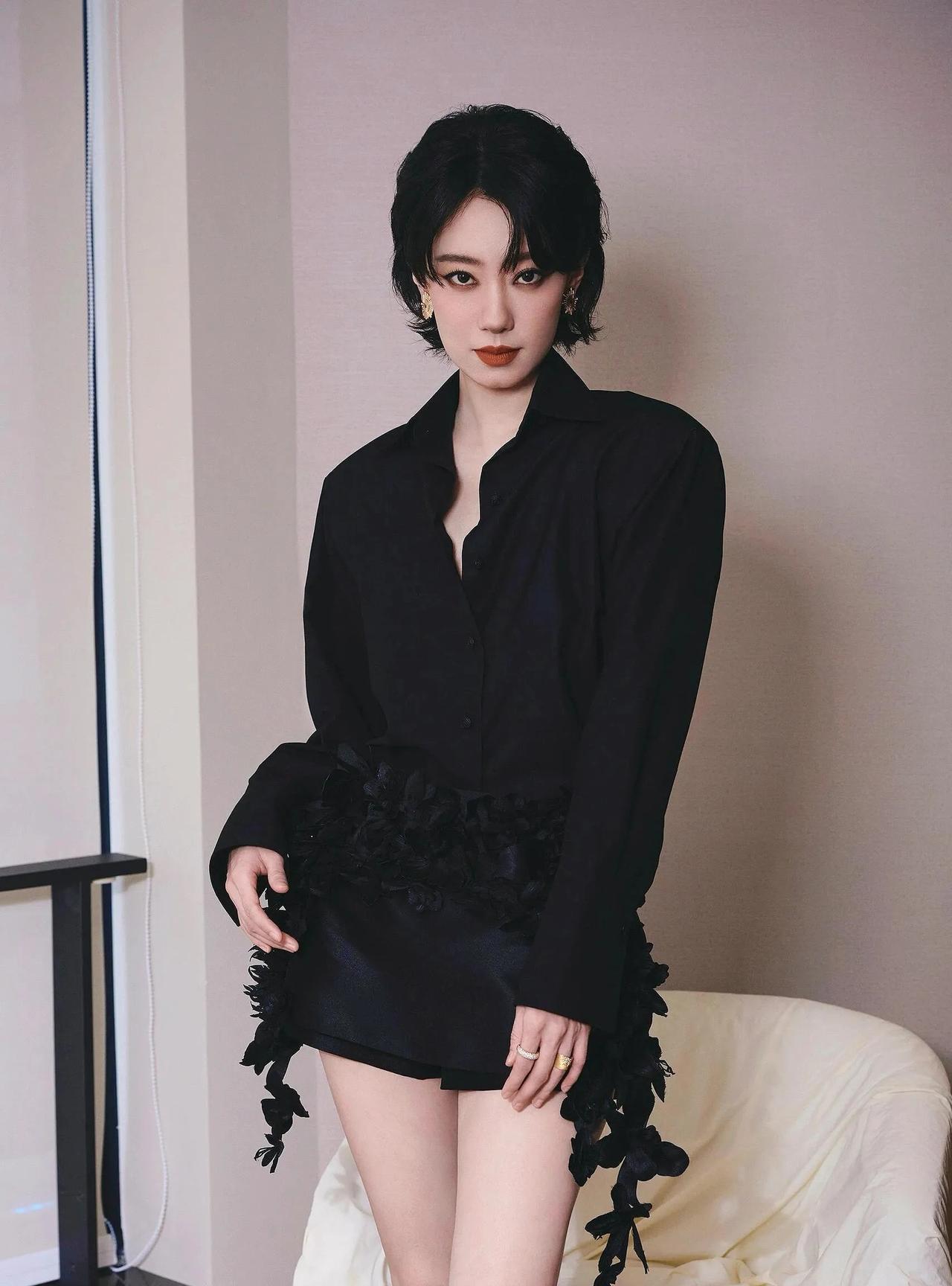 张小斐一身暗黑风穿搭，宽松黑衬衫搭配带花朵装饰的短裙，脚踩细跟黑高跟鞋，简约又有