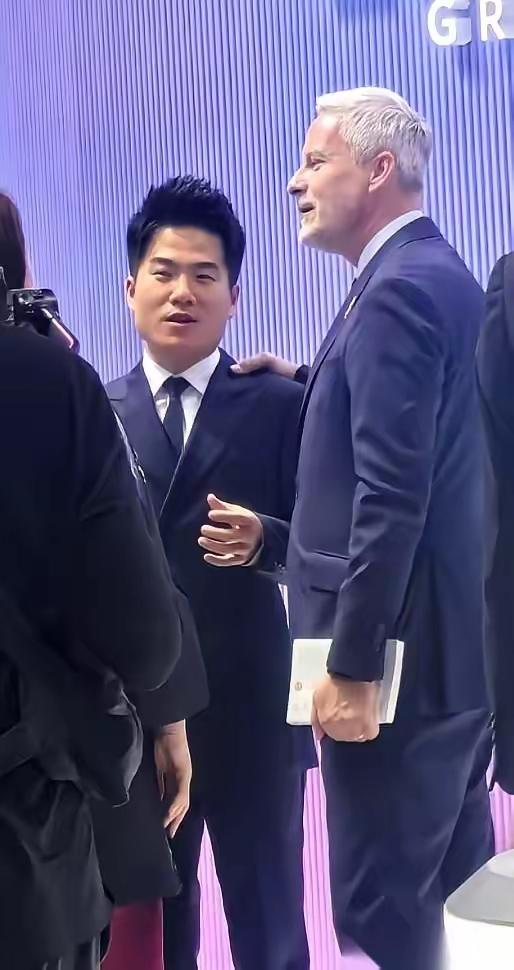 灯光刺眼。西装革履的包围圈里，那个穿休闲装的身影显得格格不入。没人知道，三分钟前