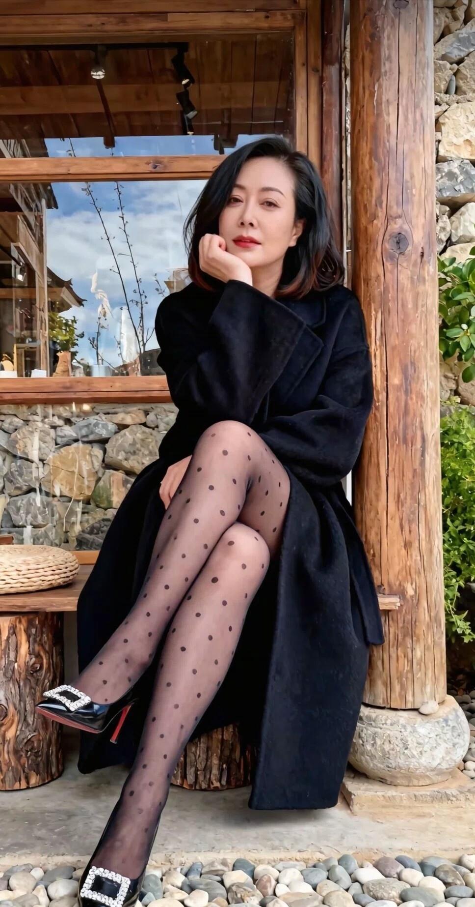 优雅黑衣女子，静坐木柱旁，黑点丝袜与高跟鞋相得益彰，自然光下更显气质。