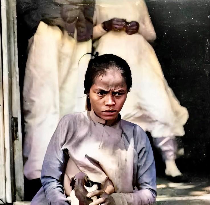 1880年，越南河内，一名年轻的越南女子正在用自己的母乳喂小狗。她坐在门前的石阶