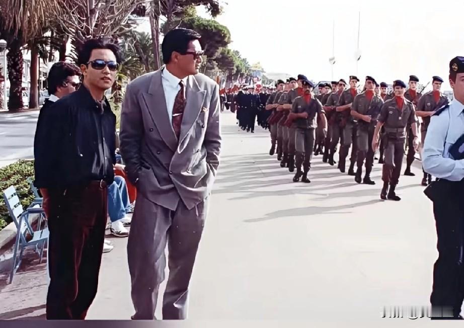 九十年代戛纳街头，黑衫少年与西装大哥并肩而立，身后的军队伍恰好成了背景。谁能想