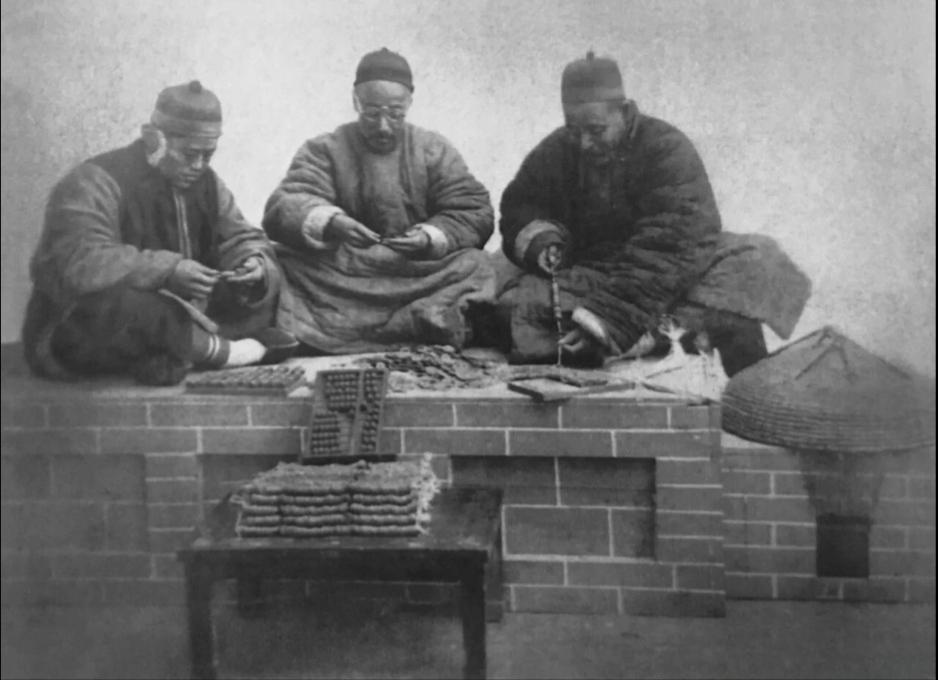 清朝历史老照片清末三个地主老财在炕头上将散铜钱串成“吊”，炕前地上的小方桌上已经