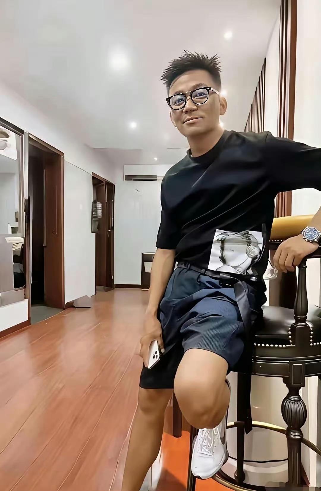 宝强穿着黑色短袖T恤，搭配深蓝色短裤和白色运动鞋，手腕上戴着一块手表，整体造型休