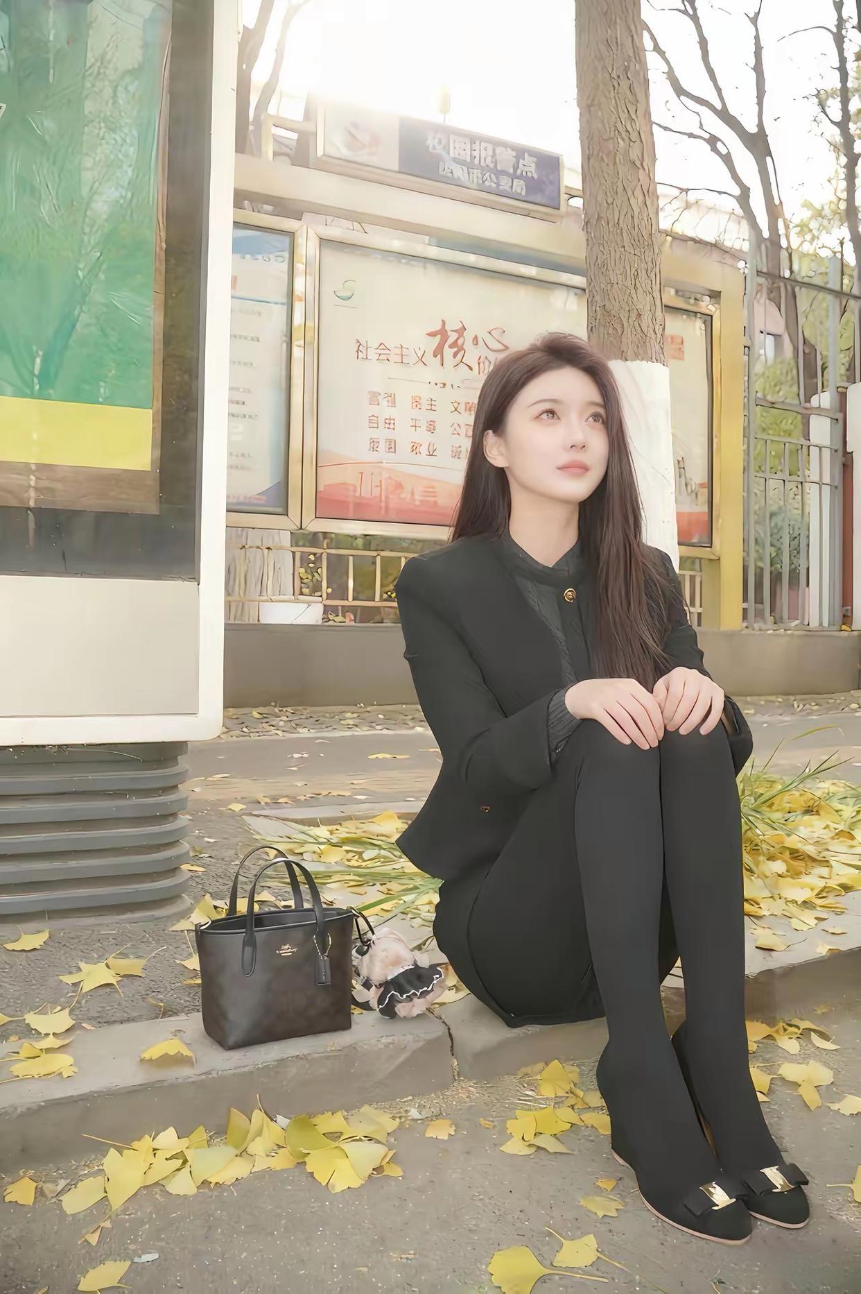 午后，黑衣少女静坐树旁，手提包旁，落叶飘零。