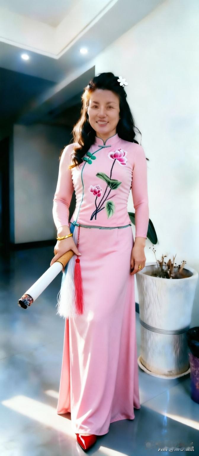 这位女士穿着粉色旗袍，微笑着站在室内。