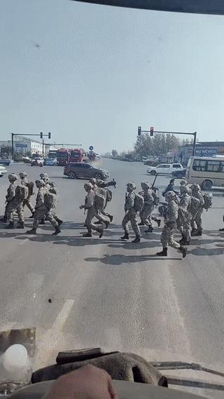 货车司机在十字路口偶遇一群军人过马路。看他们身上扛着的长枪短炮，应该是刚刚从野