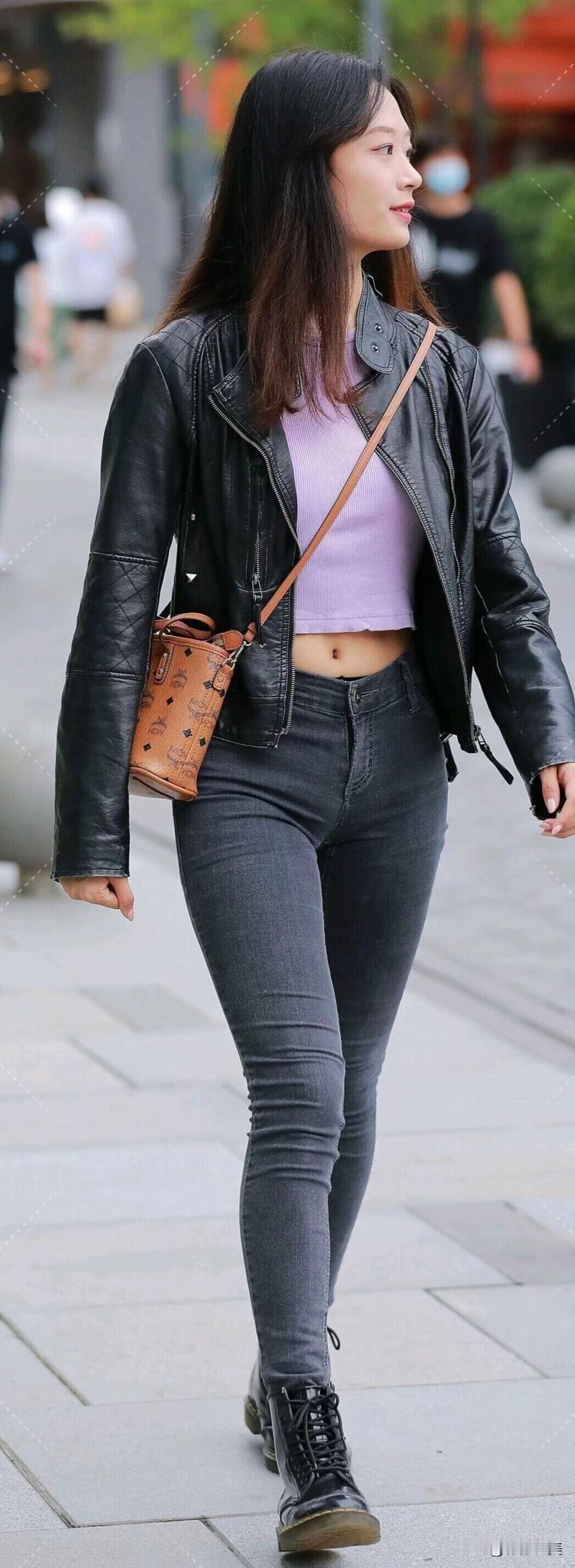 她以黑色皮夹克搭配香芋紫上衣，灰牛仔裤与马丁靴酷飒有型，挎着棕色潮包，街头行走间