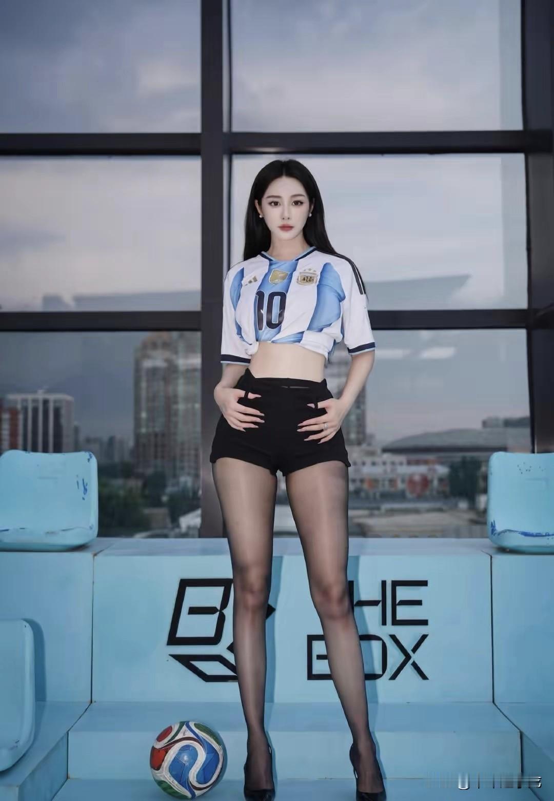美女落地窗外的城市天际线漫着柔和的暮色，蓝白条纹的阿根廷10号球衣随性挽成