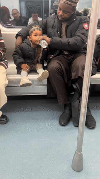 网友地铁上拍到一对黑人父子。黑人爸爸正在喂他的孩子喝水。看他孩子的肤色并不是