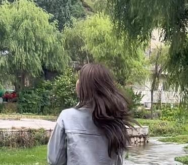 河边的风吹起她的发丝，她静静地站着，仿佛与自然融为一体。