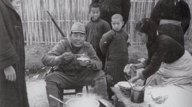 1937年12月的南京，一名日本兵背着三八式步枪、戴着军帽，坐在小板凳上，双手端