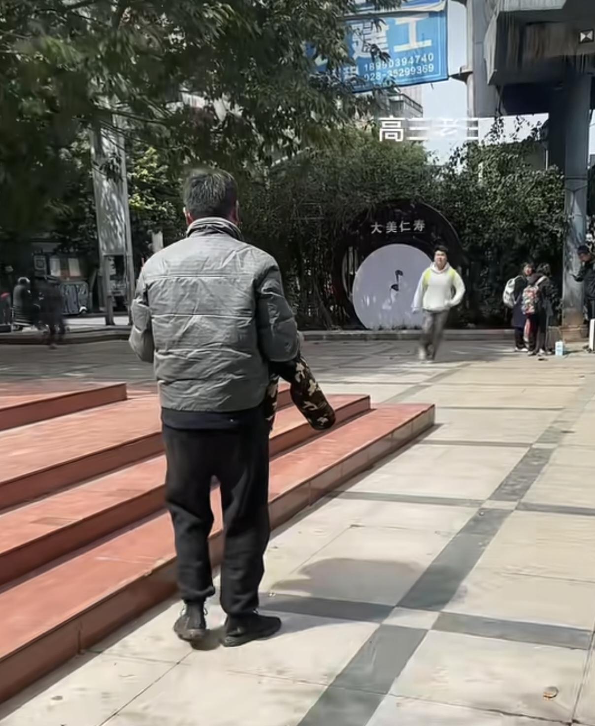 四川，父亲在高中校门口走的很慢，小心翼翼的护着怀里的棉衣，孩子从学校里出来，打开
