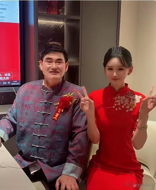 朱之文胸前佩戴红花，身穿中式唐装，参加活动时与女主持人的一张合影。网友调侃：不仔