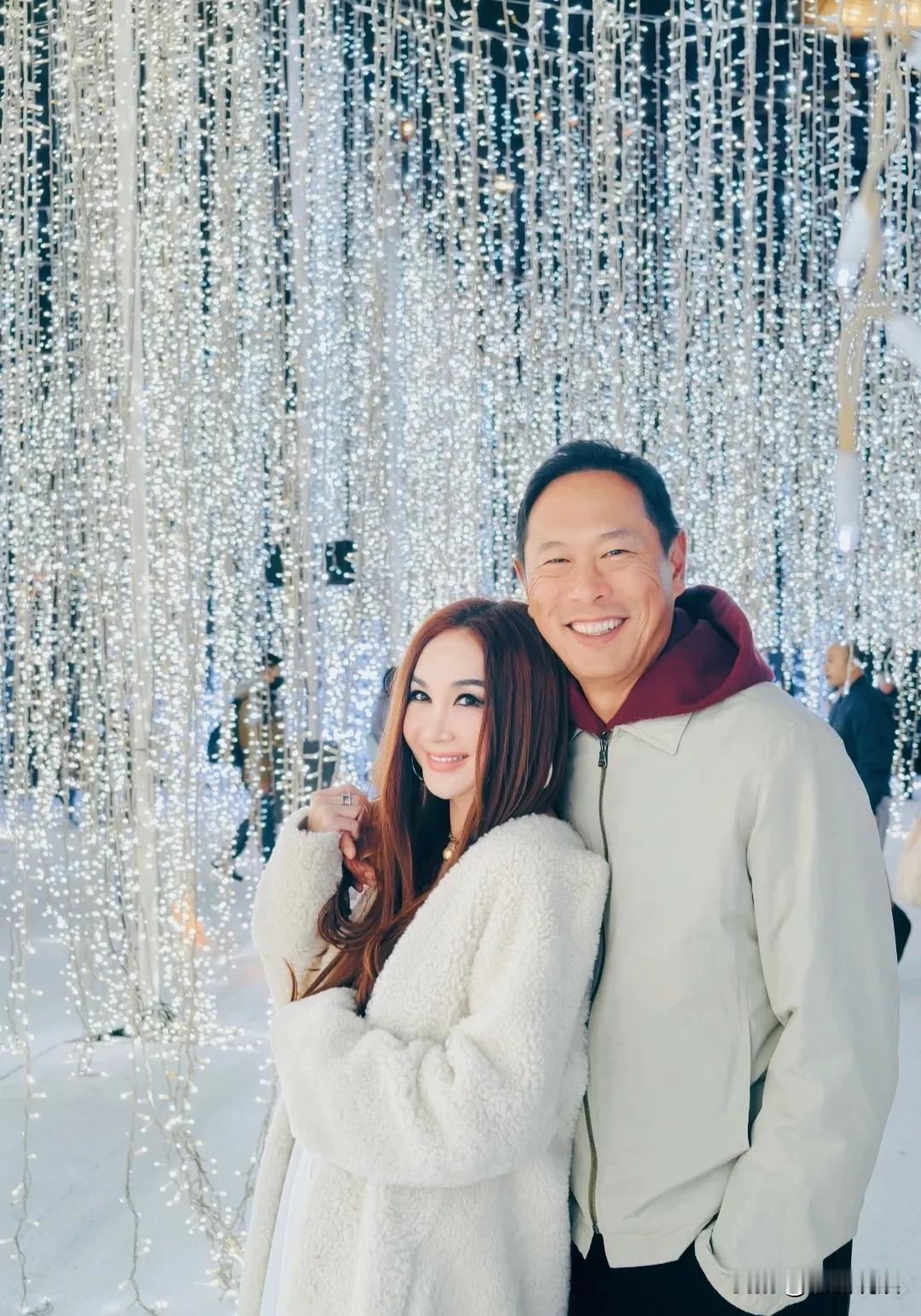 温碧霞和老公、养子一起过节，穿着一件白色毛绒长大衣，内搭低胸吊带衫，脚踩靴子。