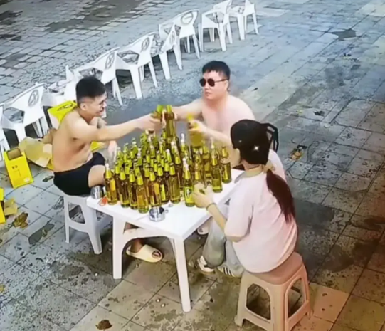 近日，在济南一家饭店的门口，两名光膀男子和一名女子，坐在一个桌前，桌上摆满了啤酒