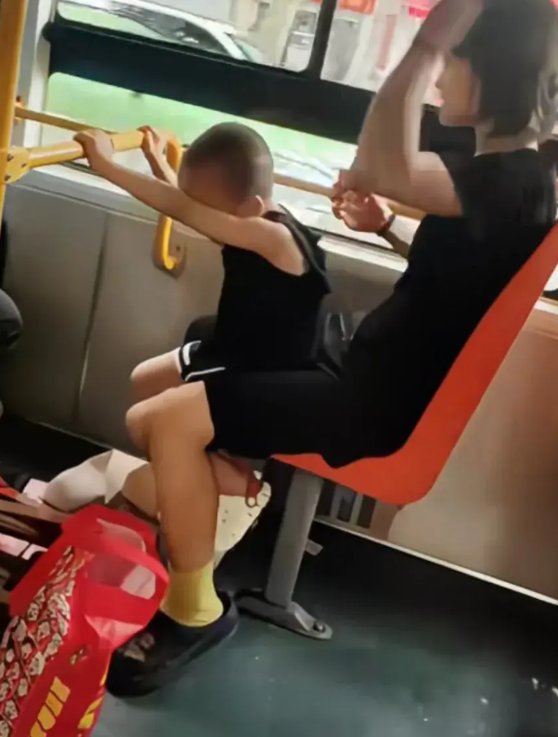 一辆公交车上，一个三四岁的小男孩和妈妈同挤在一个座位上。小男孩双手扶着前面的横杆