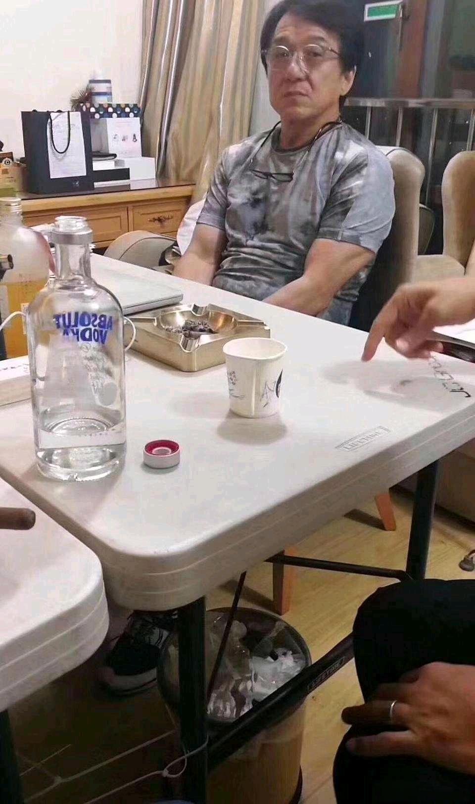 成龙的一张旧照，他与友人正在聊天的画面。成龙大哥坐在那里，戴着一副透明眼镜，