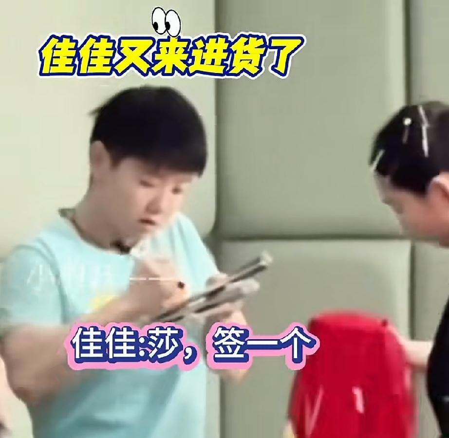 佳佳拿着球拍和秋衣在后台，看着孙颖莎签名。先签球拍再签秋衣，单单球拍就好几个。莎