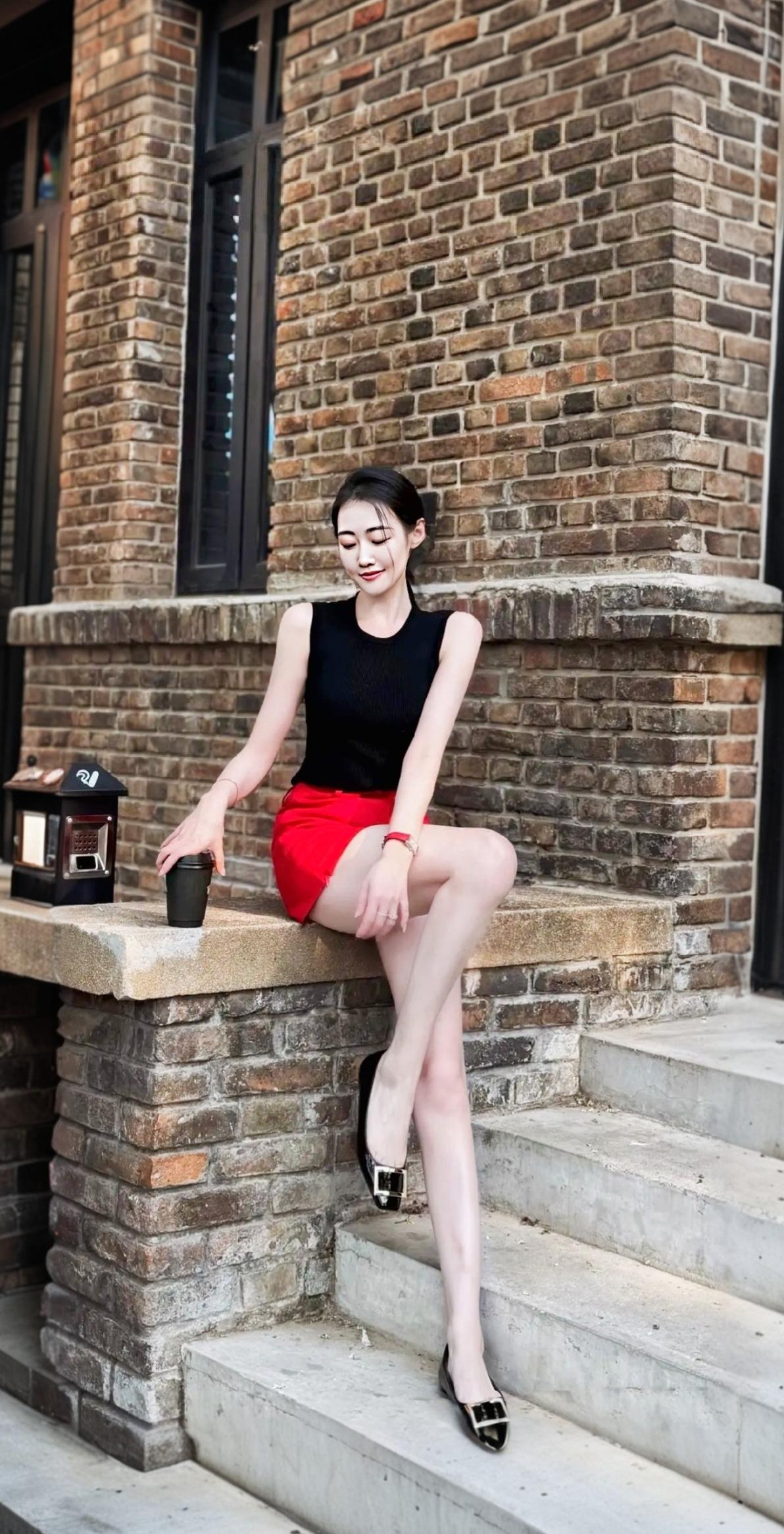 都市红裙女郎，砖墙边享受咖啡时光。