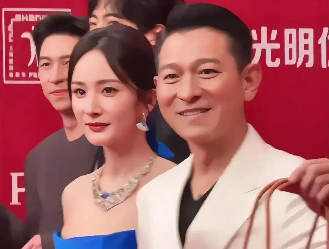 杨幂和刘德华同框，简直是新潮与经典的碰撞。杨幂身着蓝色绸缎长裙，侧边开衩露出美腿