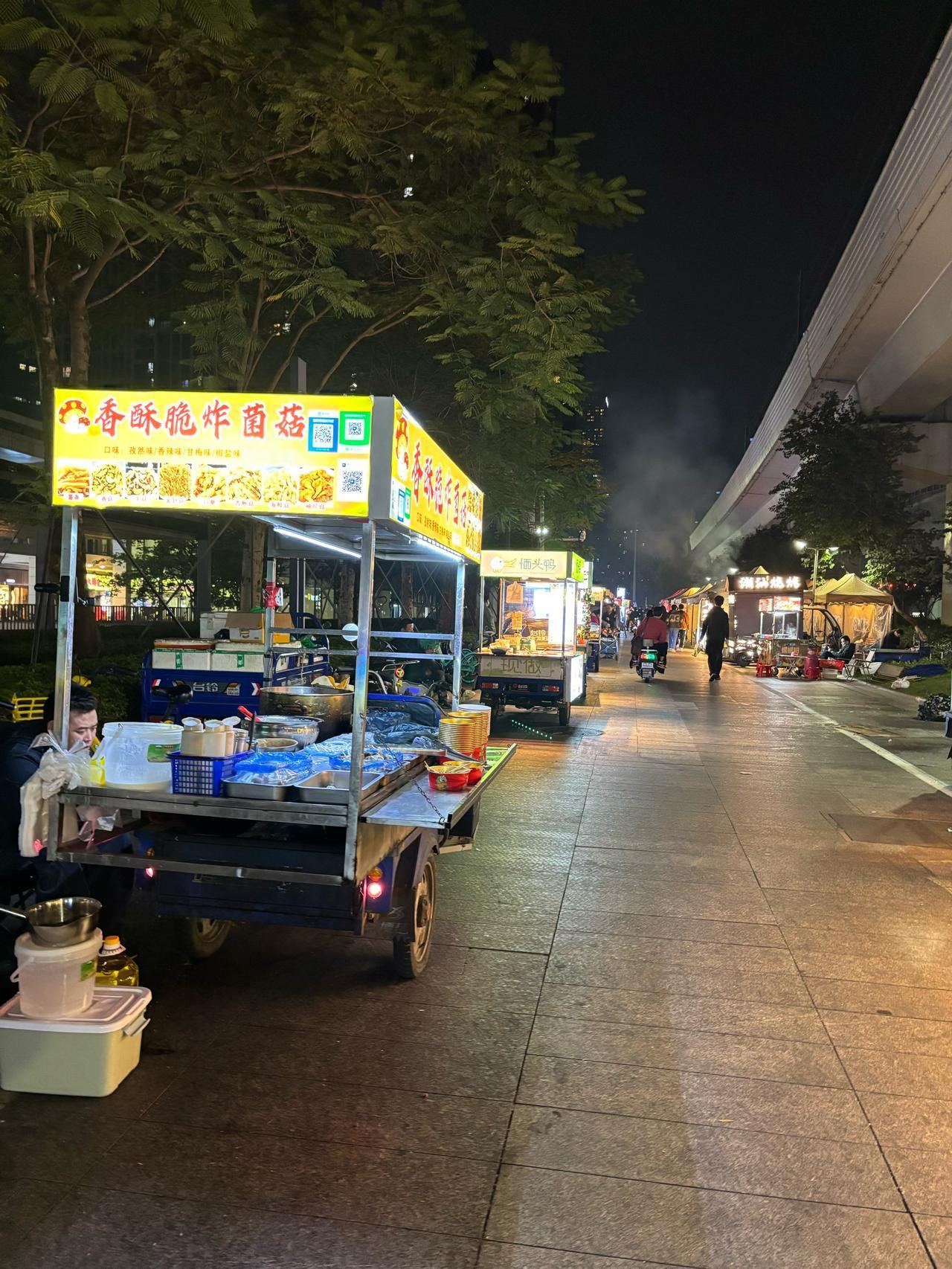 凌晨时分，街道上冷冷清清，一个大姐带着儿子和女儿在路边摆着烧饼摊。​昏黄的灯光