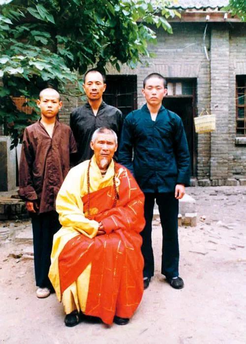 当年释永信还是个瘦小子，穿着蓝色衣服的他站在师傅的后边合影。后来穿着袈裟的他越来